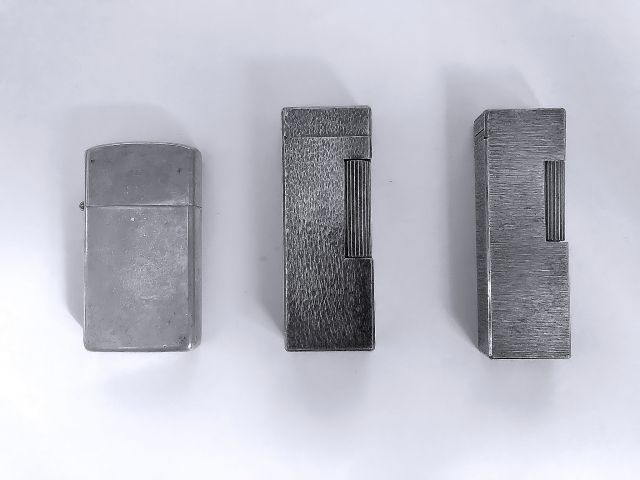 Three lighters that have been darkened to the point of needing polishing and have lost their silver luster